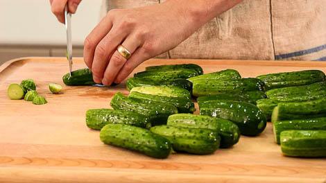 Hands cutting small cucumbers on a board