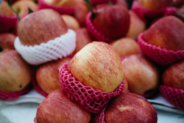 A bunch of apples in a basket with red netting