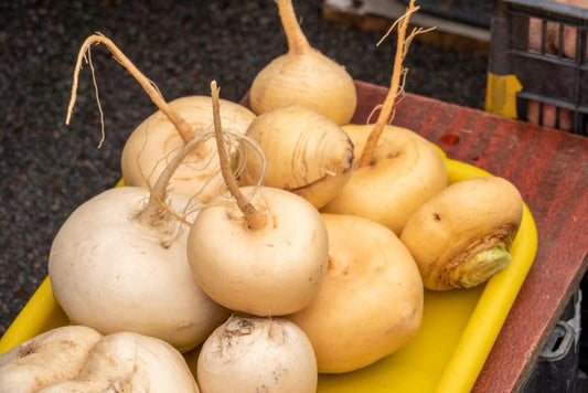 A variety of fresh turnips displayed on a yellow tray at a farmers market
