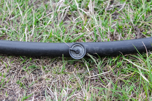 Close-up of an adjustable drip irrigation emitter installed on a flexible black plastic hose layout over green and dry grass in a backyard lawn