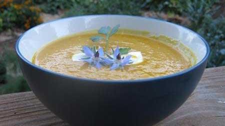 Bowl of carrot ginger soup garnished with blue flowers