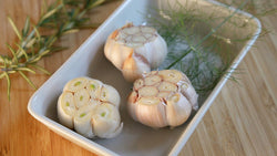 Roasted garlic bulbs and herb spread in a baking dish