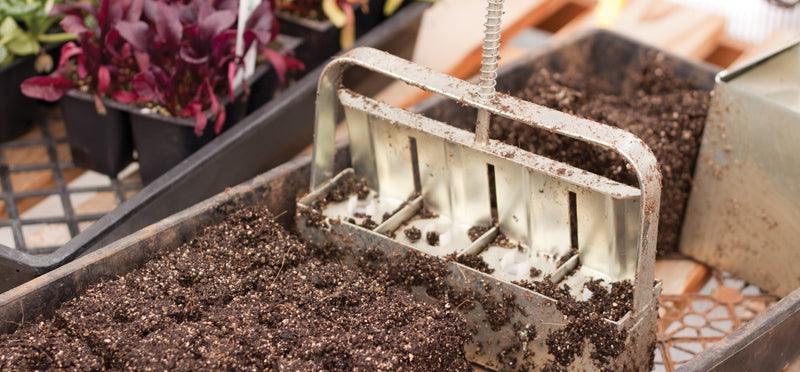 Metal soil-block maker pressed into potting soil