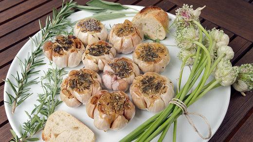 Roasted garlic bulbs surrounded by fresh herbs