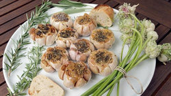 Roasted garlic bulbs surrounded by fresh herbs