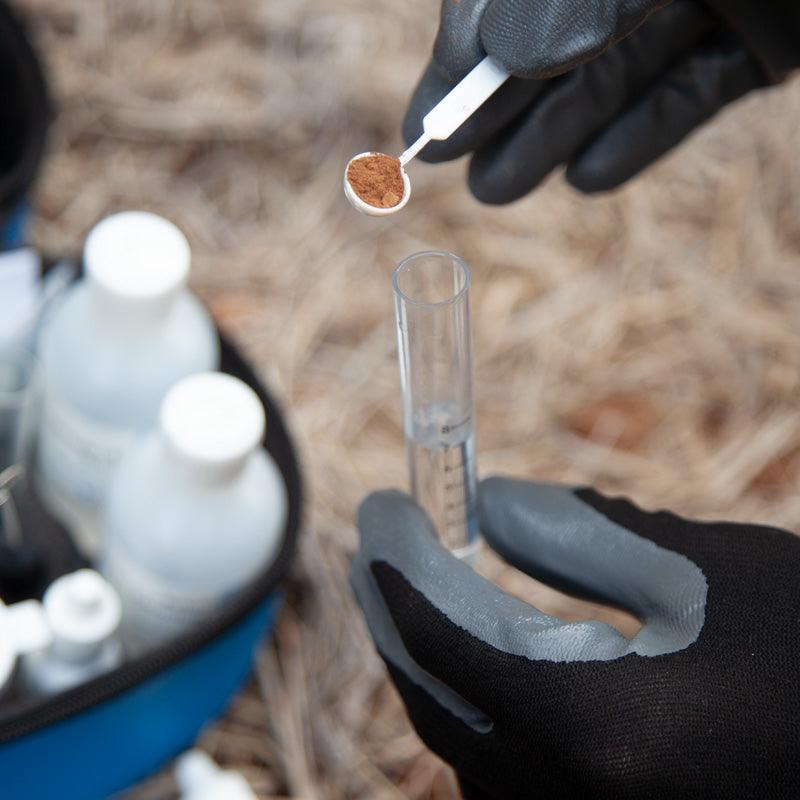 Gloved hands adding liquid to a soil-testing vial