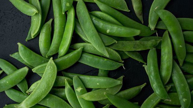 A close-up view of fresh green snap peas scattered on a dark surface, showcasing their vibrant color and texture