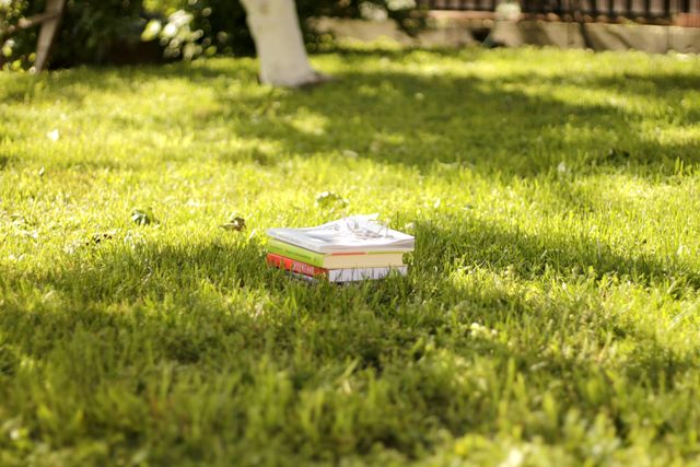 A stack of books placed on lush green grass in a sunlit garden setting