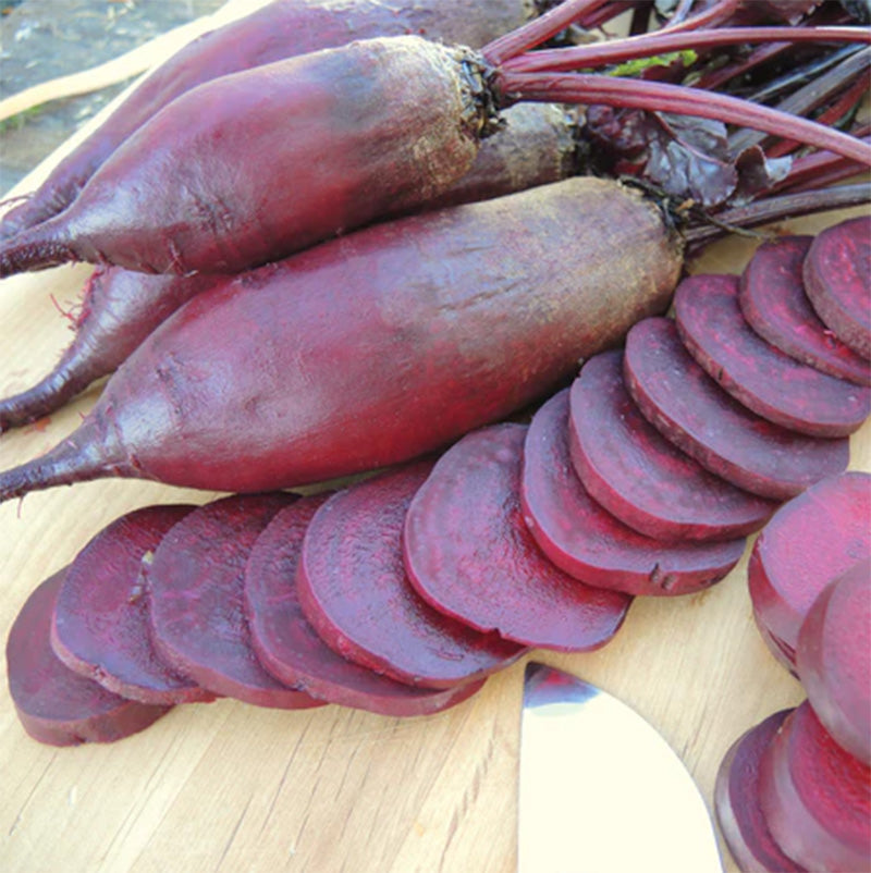 A Cutting board with whole beets as well as sliced pieces 