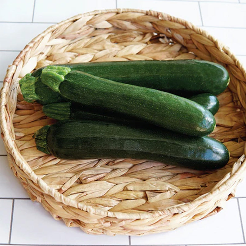 A woven basket displaying Emerald Delight Summer Squash  against a white tile background 