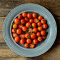 A blue grey plate displaying halved and whole Sweet Million Cherry Tomatoes, against a deep wooden plank background
