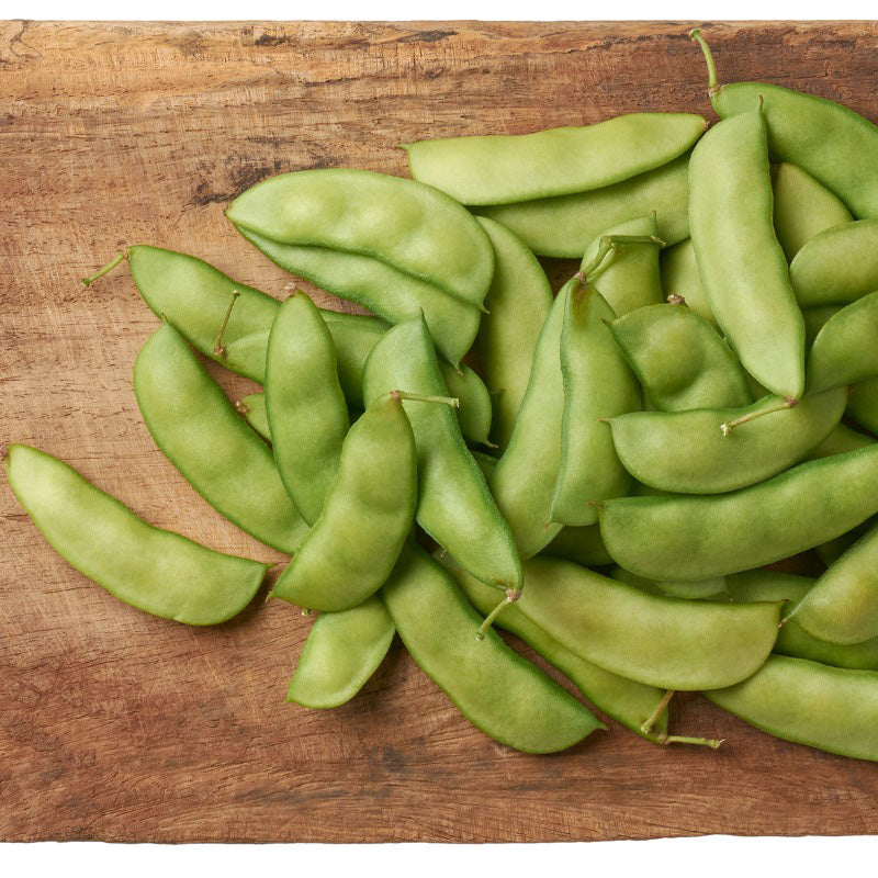 Thorogreen Lima Beans resting on a cutting board, pale green pods 