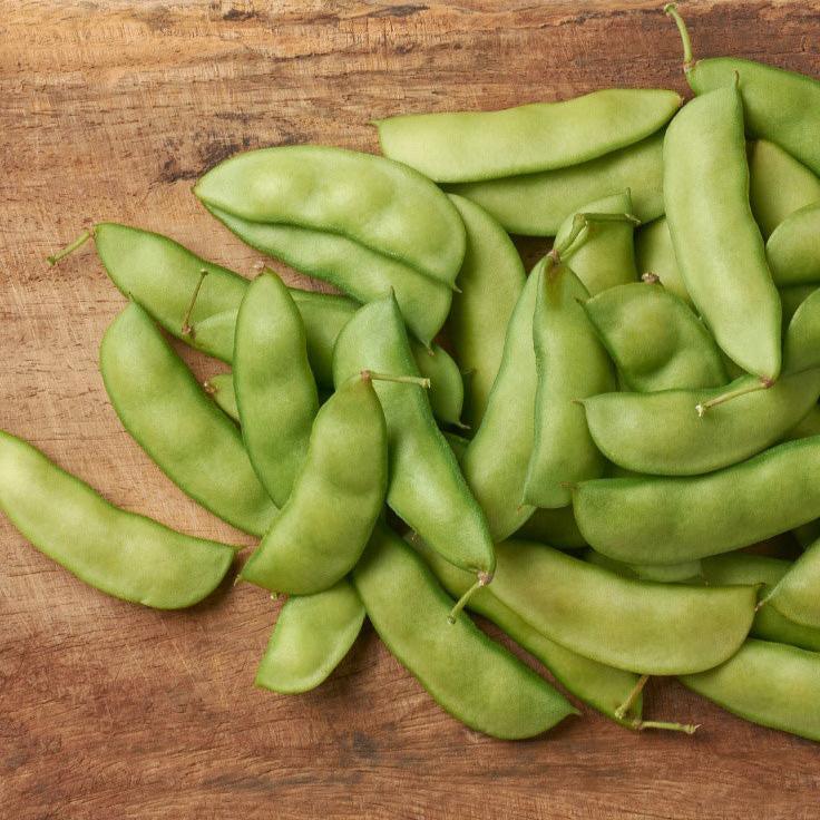 Thorogreen Lima Beans resting on a cutting board, pale green pods 