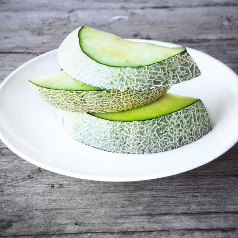 A white plate displaying fresh cut green fleshed Rocky Ford Melon 