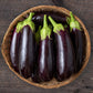 A woven basket sitting on wood planks full of deep purple Diamond Eggplants 