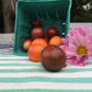 Tipped over tomato Container presenting Multicolored Bumlbebee Cherry Tomatoes, Resting next to a purple flower for contrast